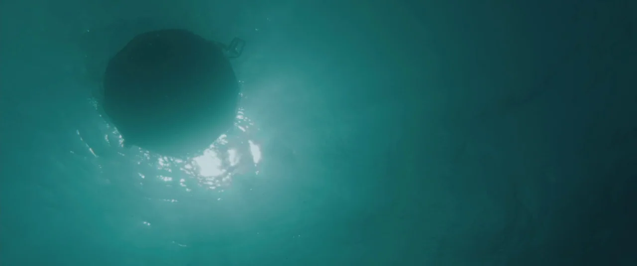 All Is Lost (2013) movie still: wide — A dark spherical buoy floats on the surface of deep turquoise ocean water. Sunlight diffuses through the…
