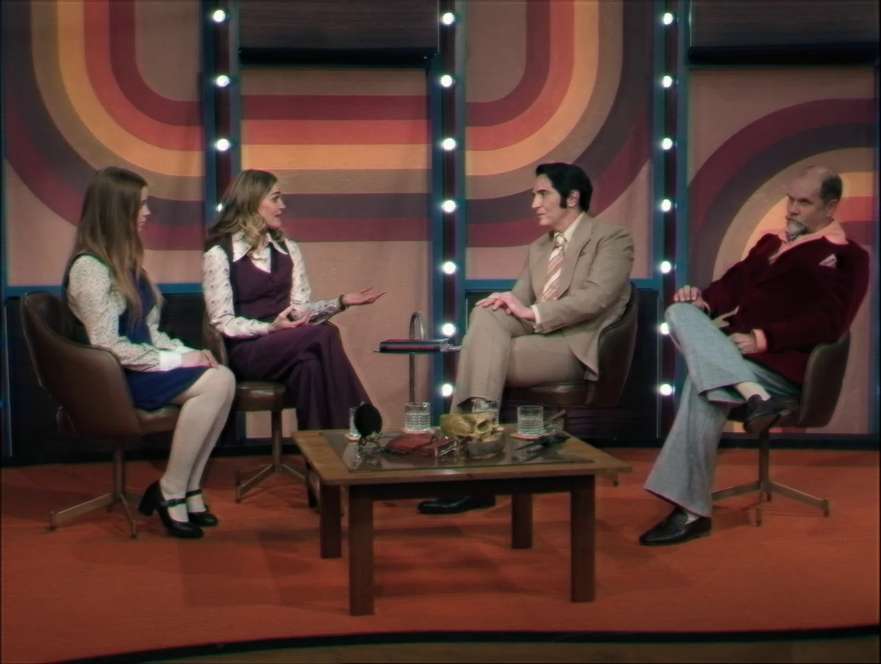 Late Night With The Devil (2023) movie still: wide — A 1970s television talk show set features patterned circular wall decor and orange carpeting.…