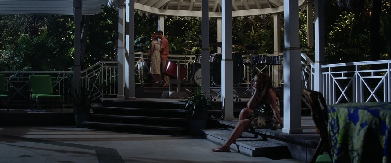 License to Wed (2007) movie still: wide — A wooden gazebo at night is surrounded by dark tropical foliage and outdoor furniture. A woman sits alone…