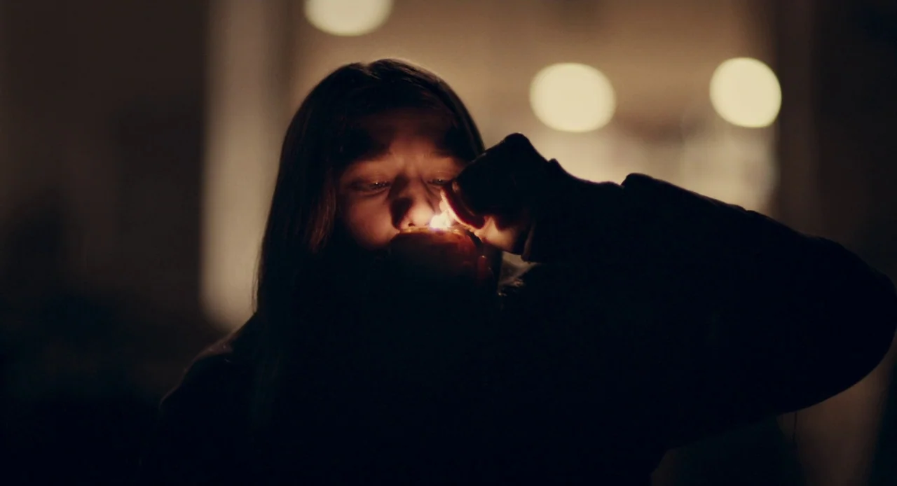 Mistress America (2015) movie still: closeup — A person stands in a dark environment with blurred circular lights in the background. The individual…