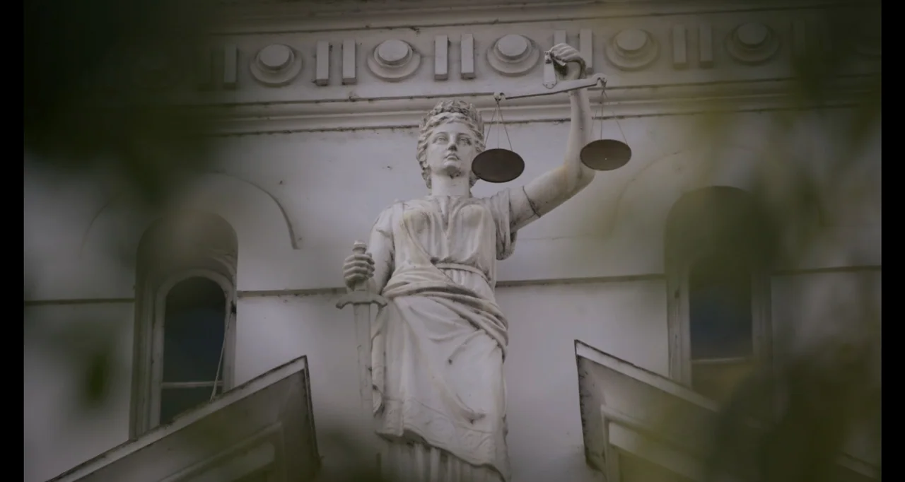 Hunted by My Husband: The Untold Story of the DC Sniper (2025) movie still: medium — A stone statue of Lady Justice is positioned on the exterior of…