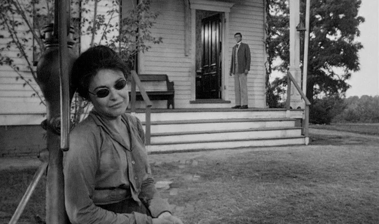 The Miracle Worker (1962) movie still: medium — A woman leans against a wooden porch pillar in the foreground. A man stands at the doorway of a…