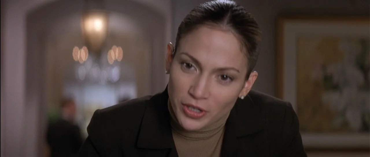 The Wedding Planner (2001) movie still: closeup — A well-lit interior hall with a chandelier visible in the out-of-focus background. A woman in a…