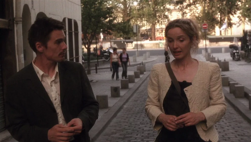 Before Sunset (2004) movie still: medium — A European cobblestone street with bollards and trees in the background during daytime. A man and a woman…