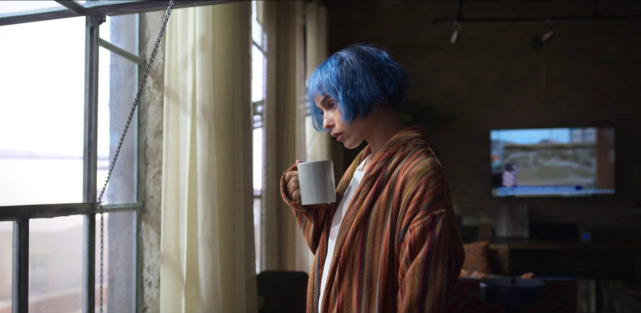 Kimi (2022) movie still: medium — A modern apartment with a large window and a television mounted on a brick wall. A woman with blue hair stands by…
