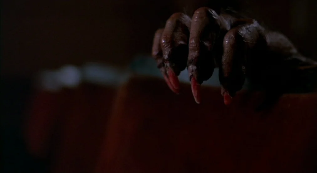 An American Werewolf in London (1981) movie still: closeup — A dark indoor setting features a textured, monstrous hand gripping the edge of…
