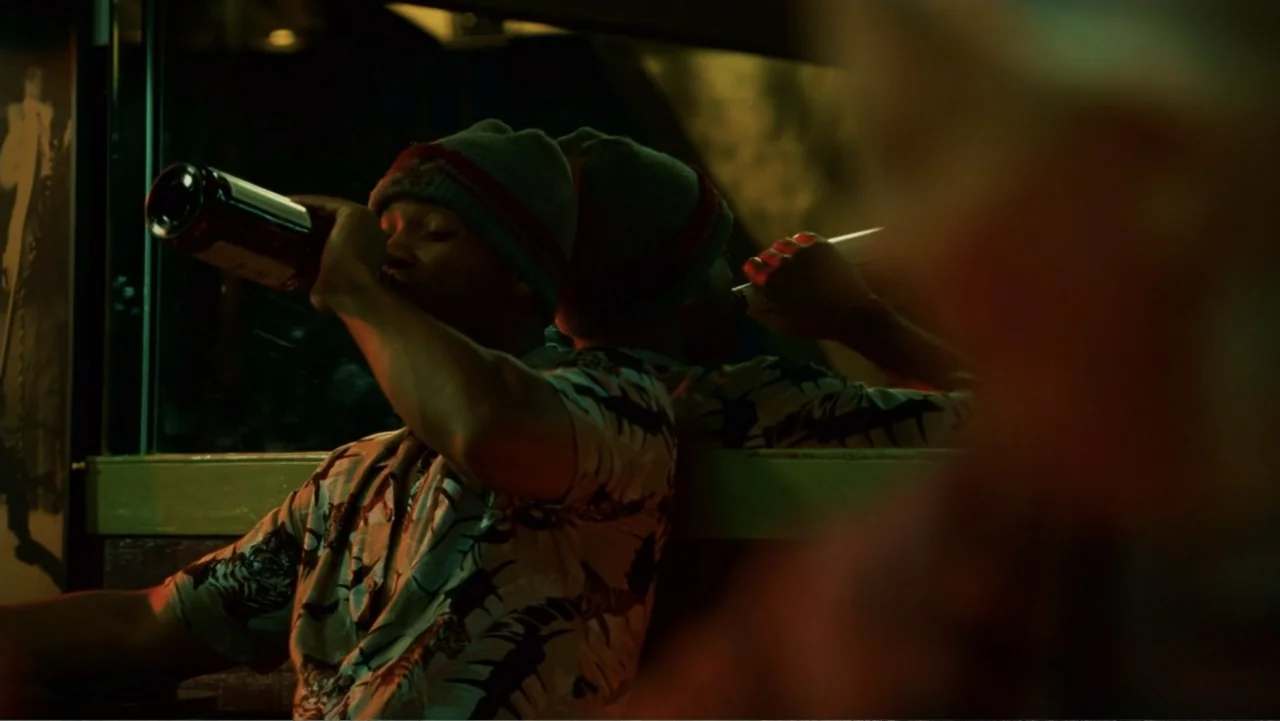Hancock (2008) movie still: medium — A dark diner booth at night with a large window reflecting the interior lights. A young man wearing a beanie…