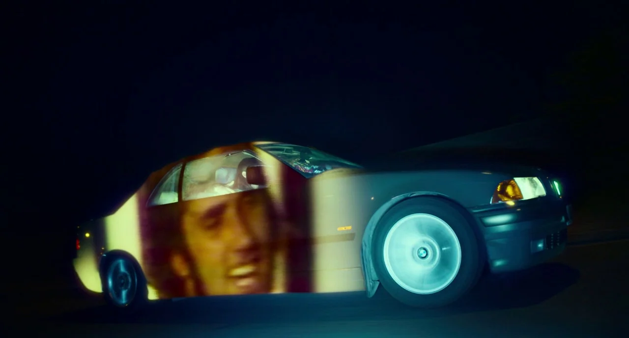 T2 Trainspotting (2017) movie still: wide — A dark, blurred road serves as the backdrop for a vehicle moving at night. A large, bright video…