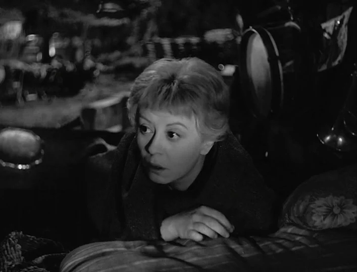 La Strada (1954) movie still: closeup — A dimly lit room contains a bed with a patterned pillow visible in the foreground. A woman with short hair…