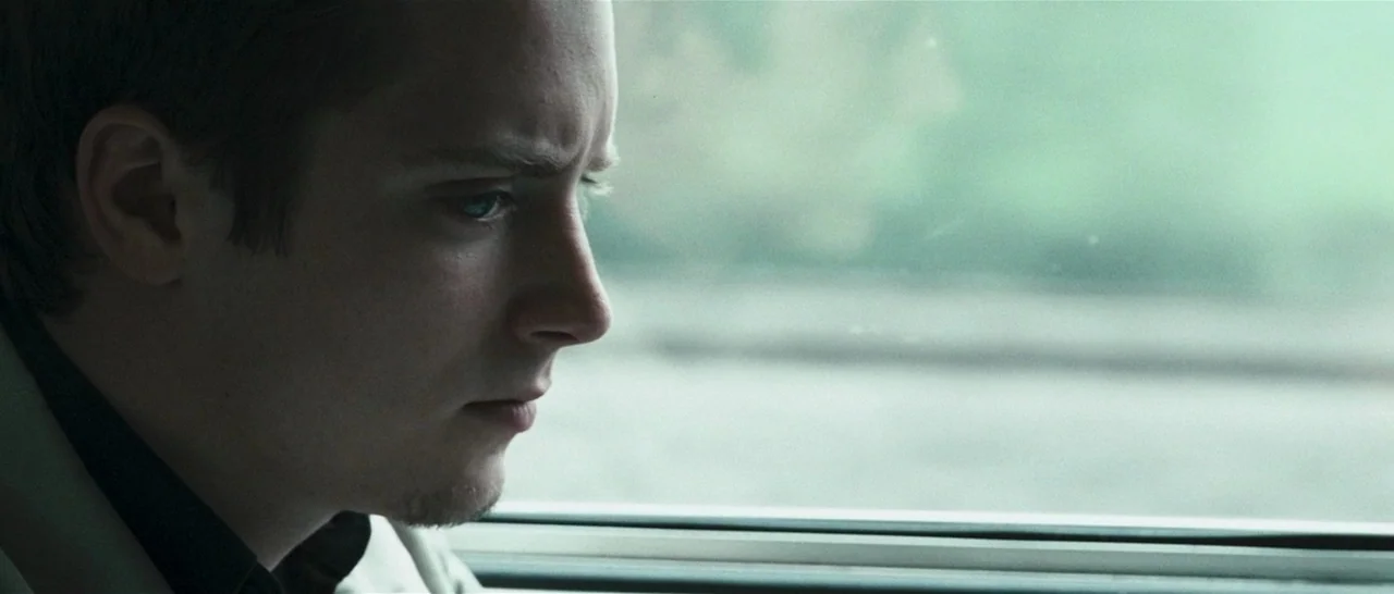 Green Street (2005) movie still: closeup — A man sits inside a train car next to a window during the day. The man gazes outward at the passing…