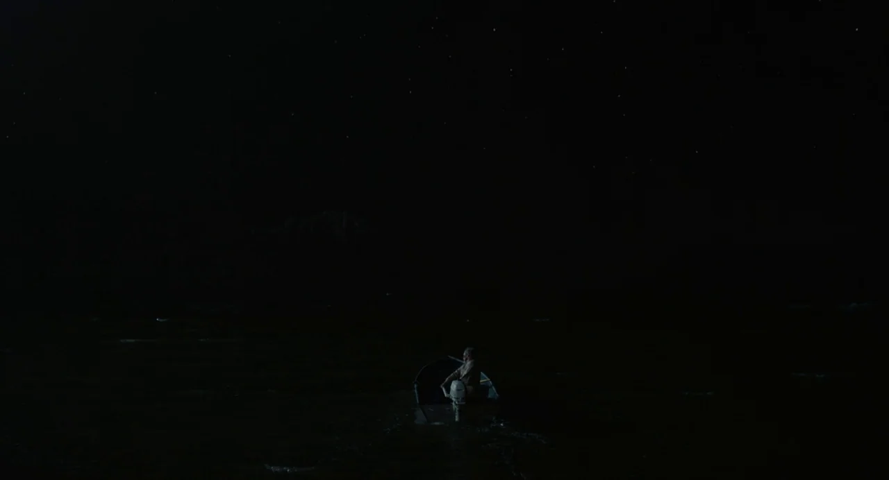 Beau Is Afraid (2023) movie still: wide — A vast expanse of dark water sits under a night sky full of stars. A lone man sits in a small boat moving…