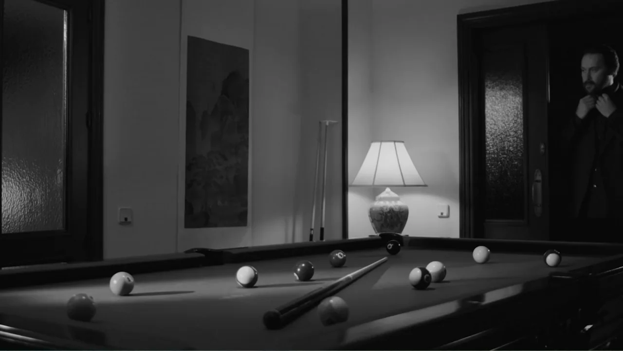 Creditors (2025) movie still: medium — A dim room contains a pool table scattered with balls and a cue stick. A man stands in the shadow of a…