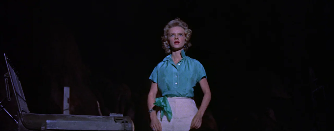 Bad Day At Black Rock (1955) movie still: medium — A woman stands alone in an undifferentiated dark exterior at night. She looks upwards with a…