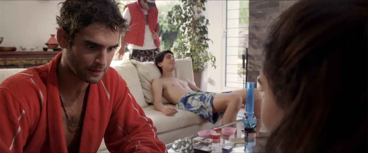 High Five (2004) movie still: medium — A living room features a white sofa, a glass coffee table, and large windows. A man in a red bathrobe looks…