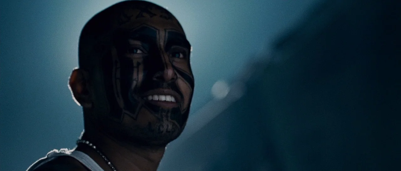 Sin Nombre (2009) movie still: closeup — An outdoor night environment with a dark, indistinct backdrop behind the main subject. A man with facial…