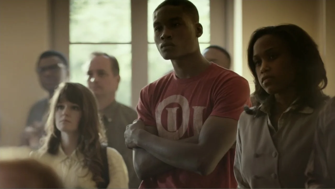 Confirmation (2016) movie still: medium — A group of diverse young adults are gathered in an indoor space with windows. The man in the red shirt…
