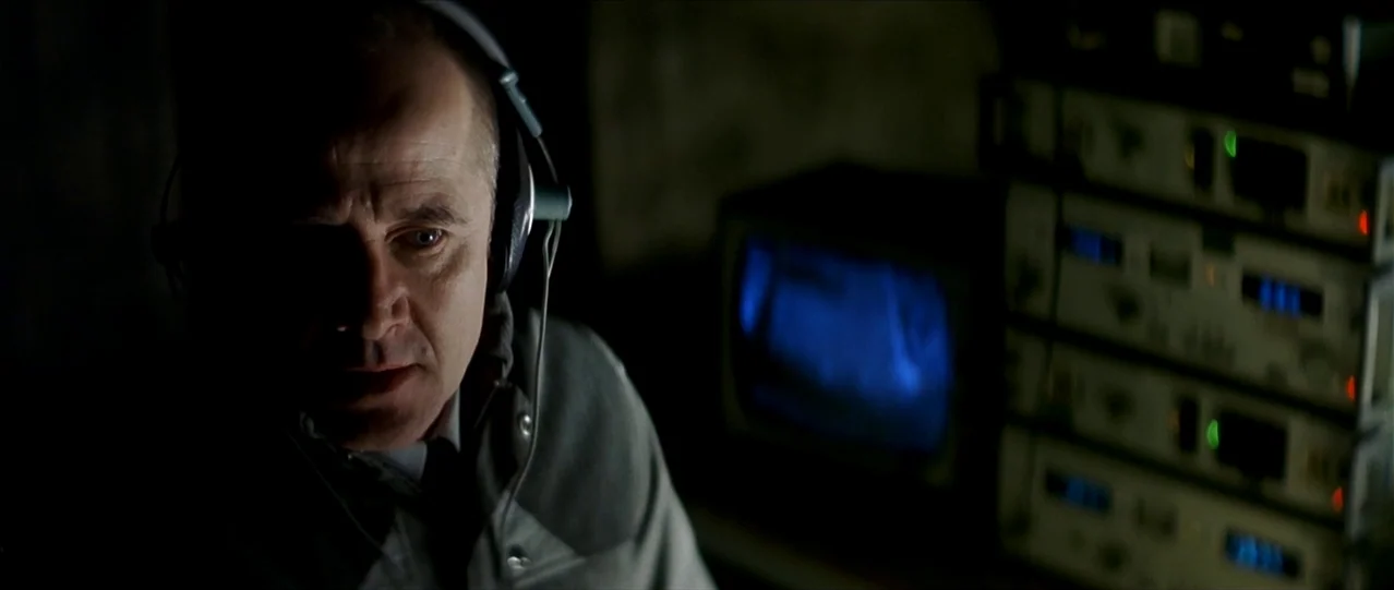The Lives of Others (2006) movie still: closeup — A dimly lit room is filled with stacked audio-visual equipment and monitoring screens. A…