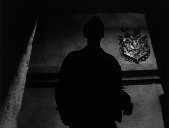 Hour of the Wolf (1968) movie still: medium — A dark stone interior features a prominent carved crest on the back wall. A man stands in the…