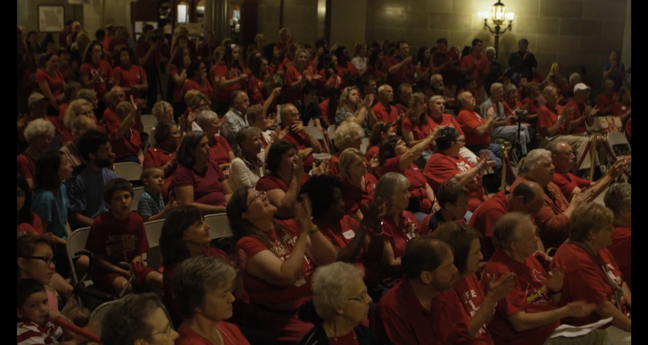 Abortion: Stories Women Tell (2016) movie still: wide — A crowded auditorium filled with people sitting in rows of white folding chairs. Many…