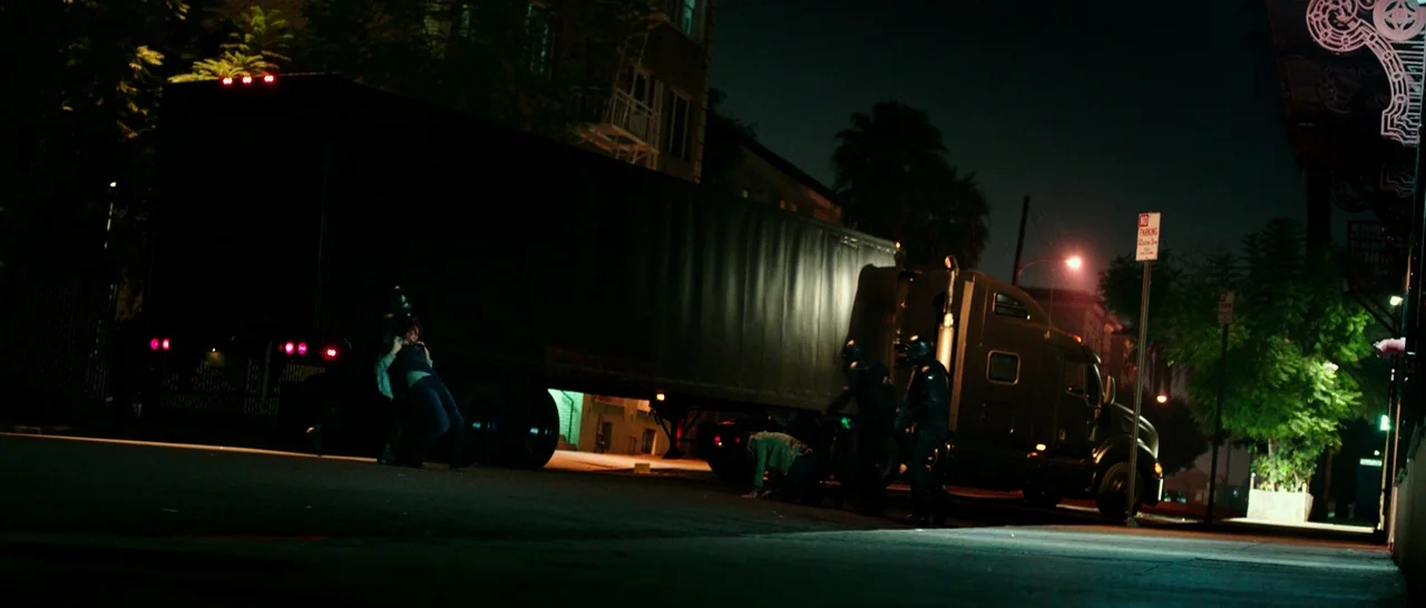 The Purge: Anarchy (2014) movie still: wide — A dark night on a city street features a large semi-truck parked near the curb. Several figures in…