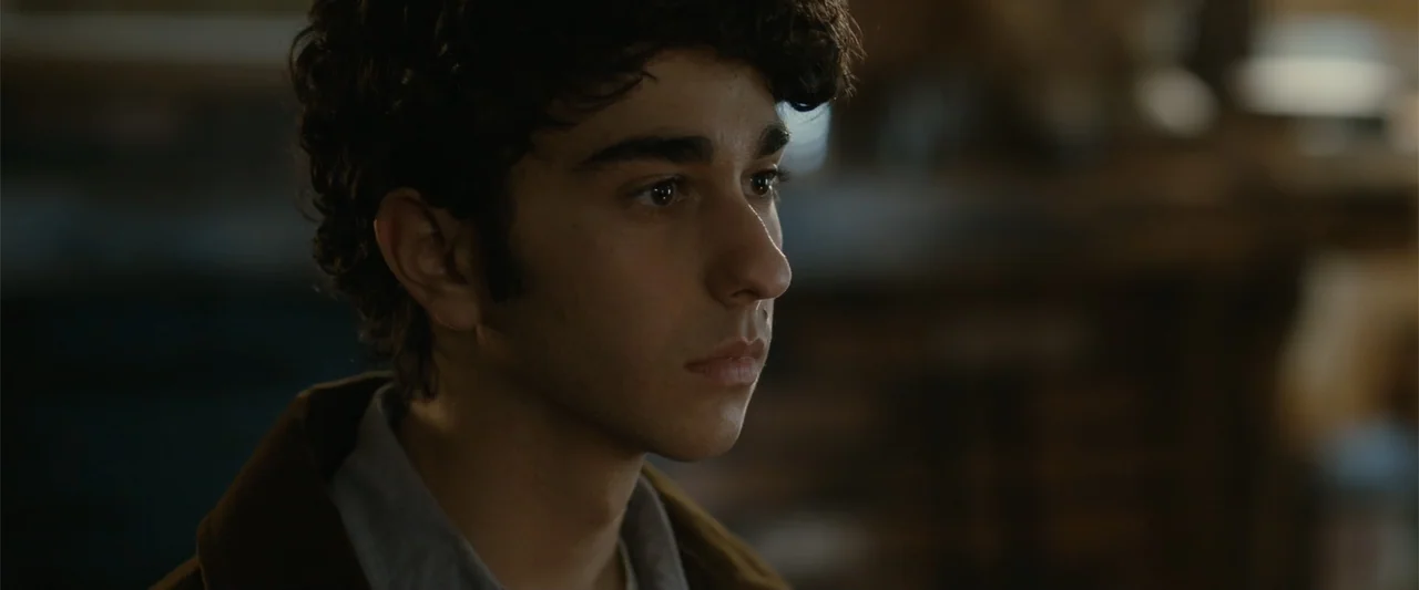 Coming Through the Rye (2016) movie still: closeup — A dimly lit interior space with an indistinct dark background. A young man with dark curly hair…