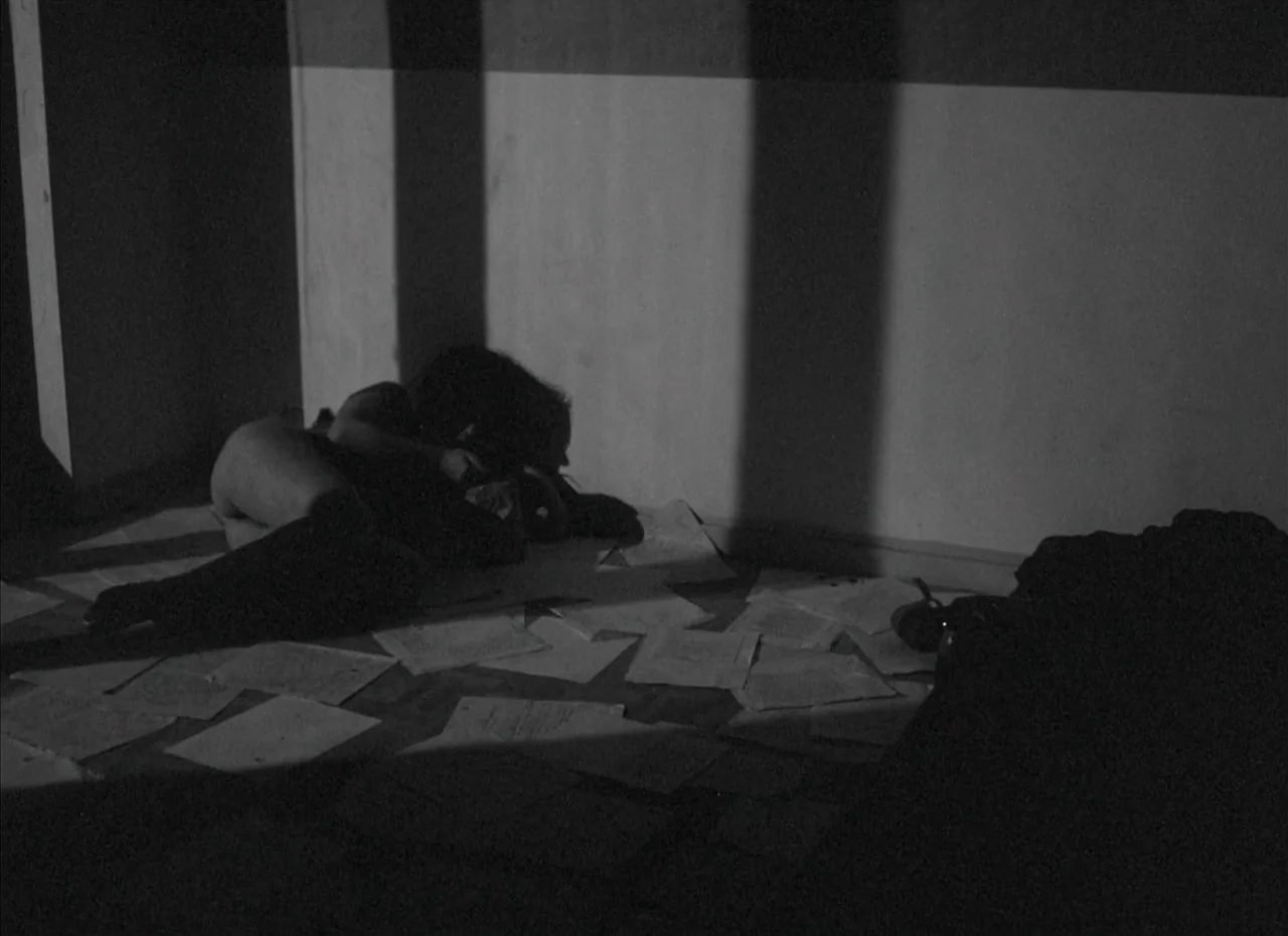 Je Tu Il Elle (1974) movie still: medium — A dimly lit interior space features bare walls and a sparse, dark floor. A person lies on the ground,…