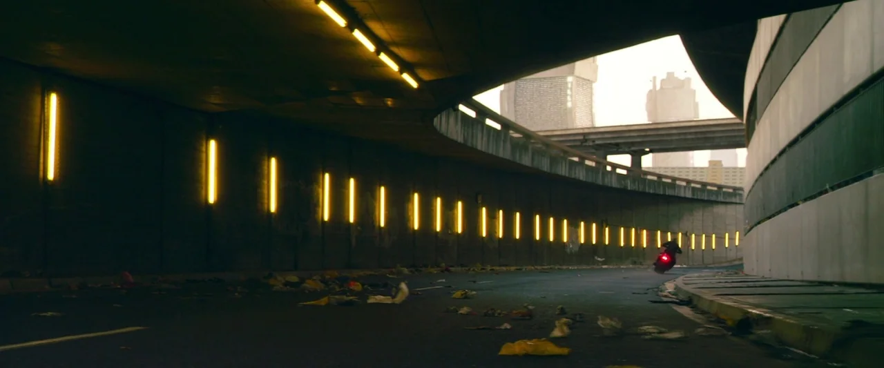 Dredd (2012) movie still: wide — An expansive concrete underpass features rows of vertical yellow fluorescent lights along curved walls. Debris…