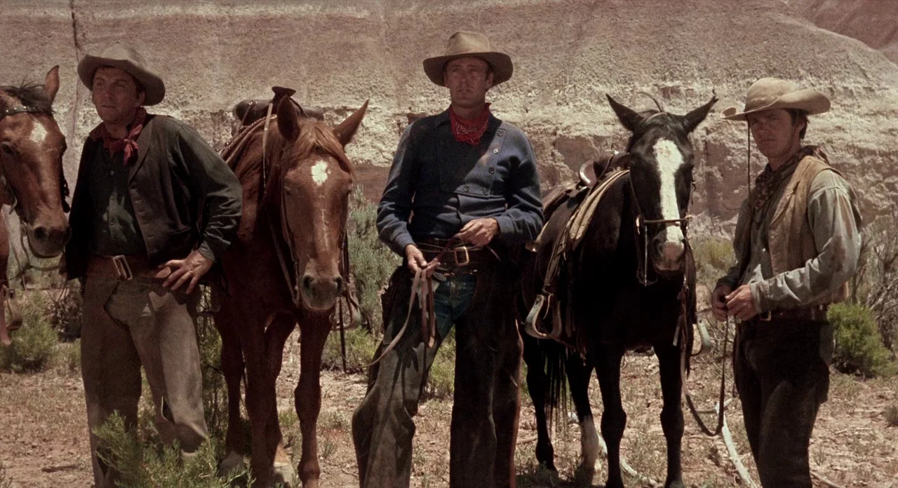 Ride In The Whirlwind (1966) movie still: fullbody — Three cowboys stand in a dry, sun-baked landscape with a beige rock formation background. Each…