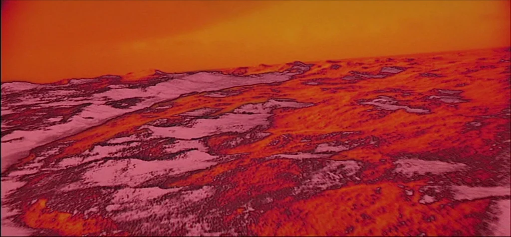 2001: A Space Odyssey (1968) movie still: establishing — An alien landscape consists of rocky, undulating terrain under a dense orange-tinted…