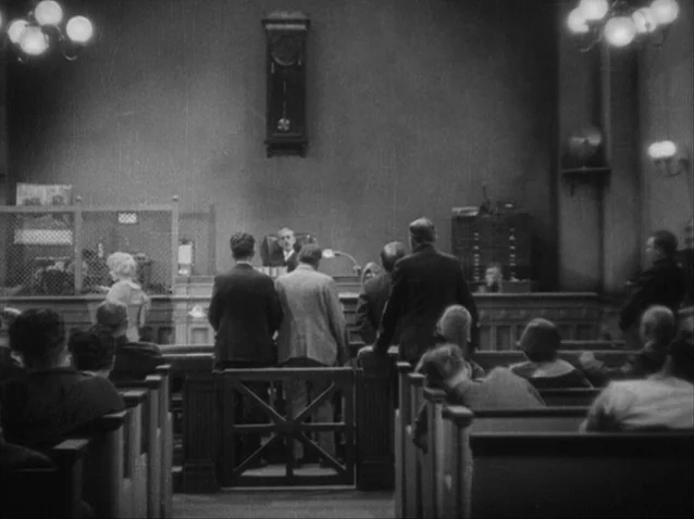 The Docks of New York (1928) movie still: wide — An interior courtroom features rows of wooden benches occupied by several people from behind. A…