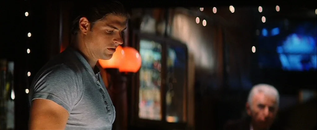 Magnolia (1999) movie still: medium — A dimly lit bar features a man in a grey shirt facing toward the center. An older man sits in the shadows…