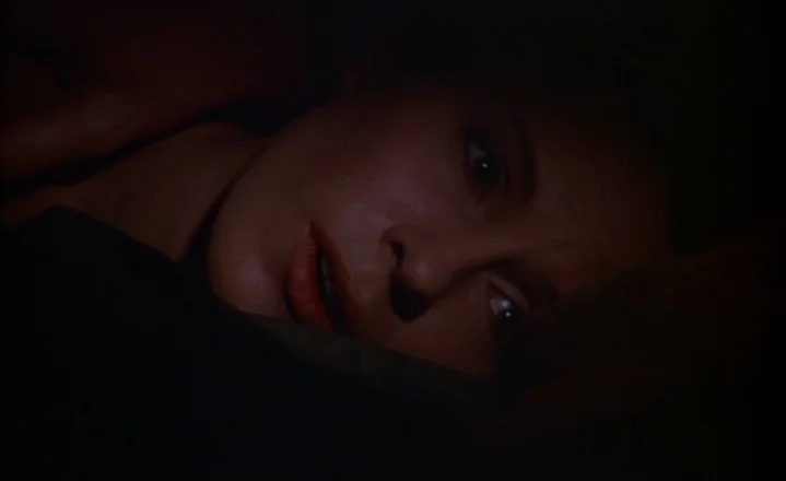 The Passion of Anna (1969) movie still: closeup — A dark, dimly lit indoor space at night. A woman is seen in a close-up lying on a bed with her…