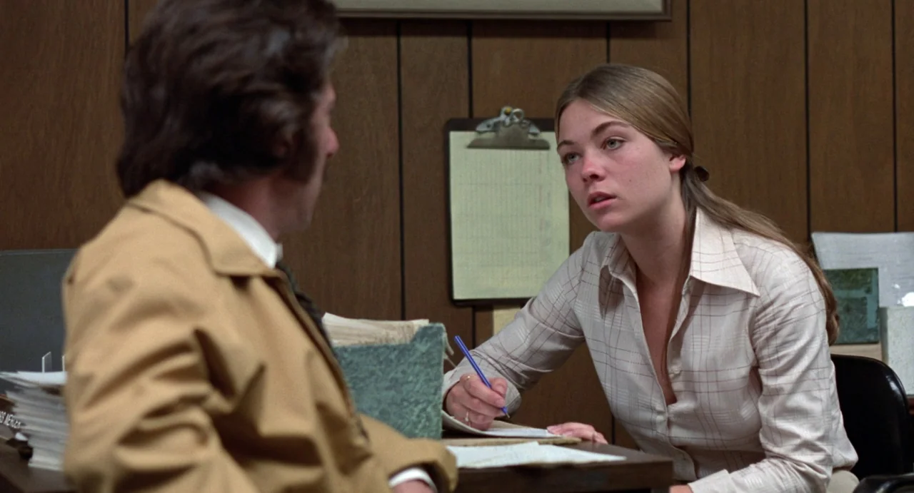Straight Time (1978) movie still: medium — An office space features dark wood paneling and a wall-mounted metal clipboard. A young woman sits at a…
