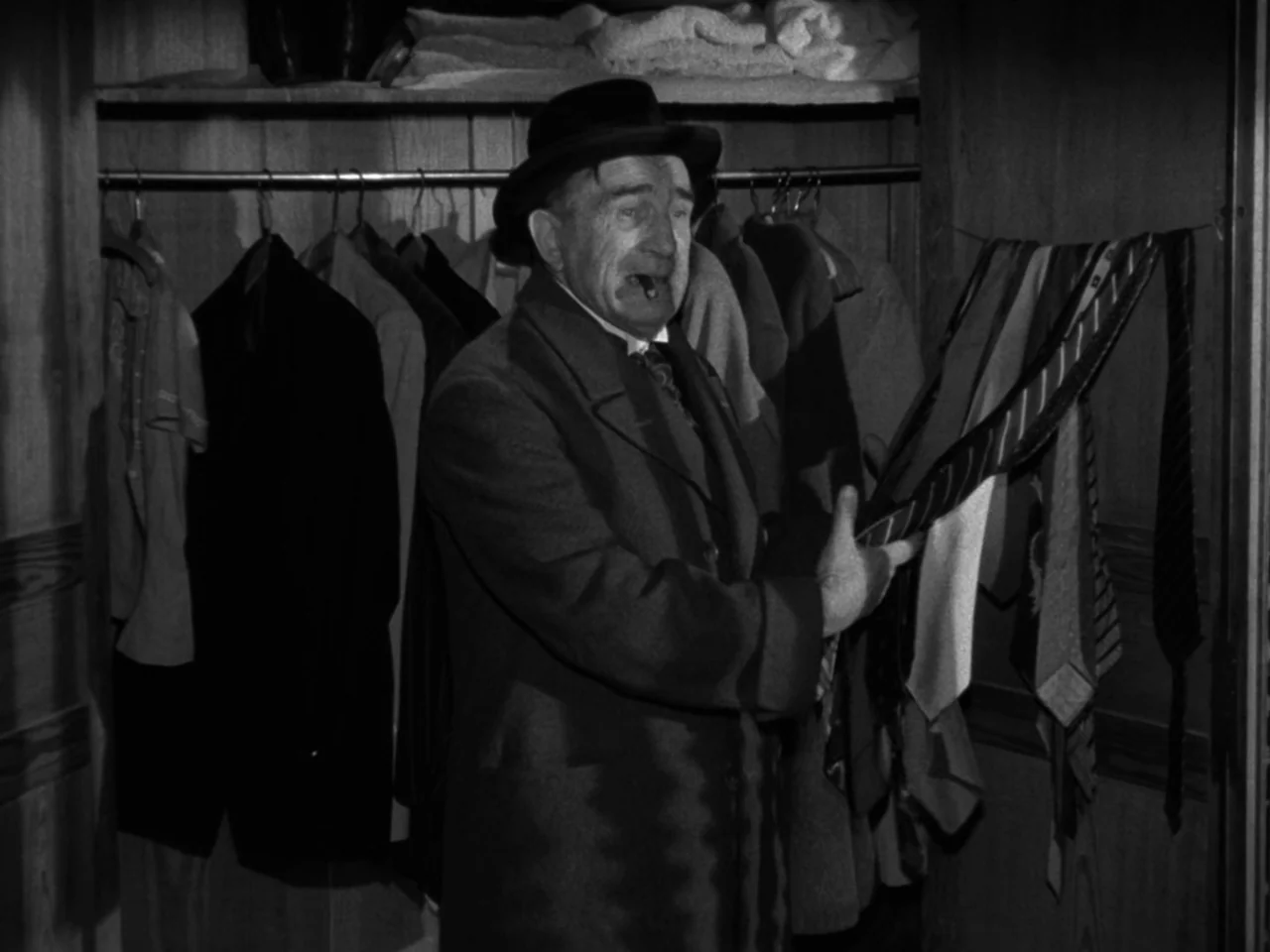 Diabolique (1955) movie still: medium — A wooden closet interior filled with hanging coats and rows of assorted neckties. An elderly man in a formal…