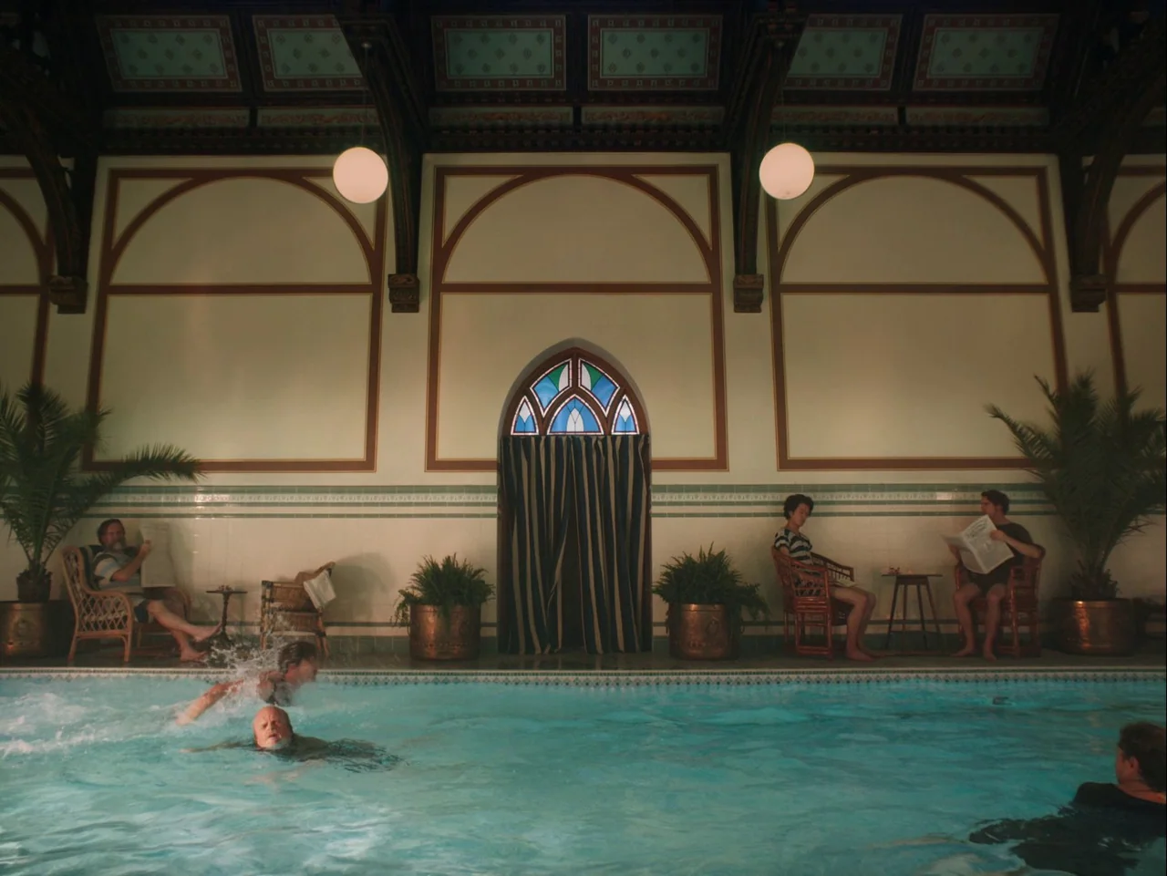 The Electrical Life of Louis Wain (2021) movie still: wide — An indoor swimming pool room features high ceilings, arched wall motifs, and potted…
