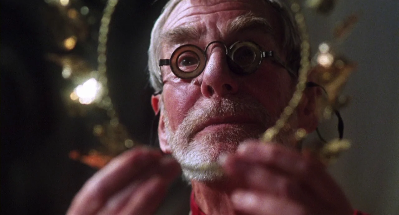 Caravaggio (1986) movie still: closeup — An elderly man examines a metallic gold halo object inside a dimly lit interior space. He holds the thin…