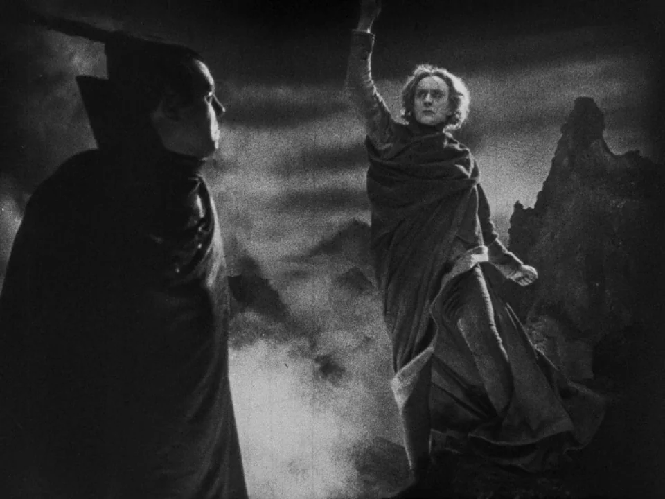 Faust (1926) movie still: fullbody — A bleak, rocky mountain landscape under a dark, cloudy sky is depicted theatrically. One man in a draped robe…