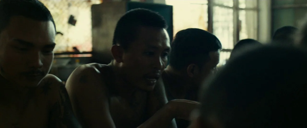 A Prayer Before Dawn (2017) movie still: medium — A group of shirtless men sit together in a room with industrial windows. They are engaged in a…