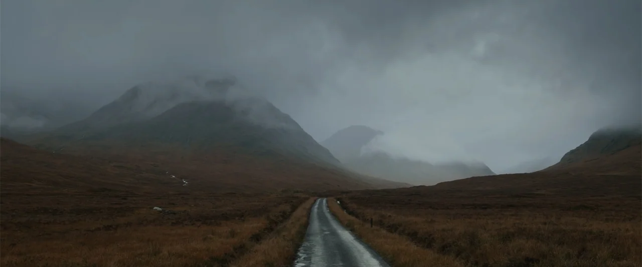 My Son (2021) movie still: wide — A wet single-lane paved road leads into a misty mountain valley. The surrounding hills are covered in brown…