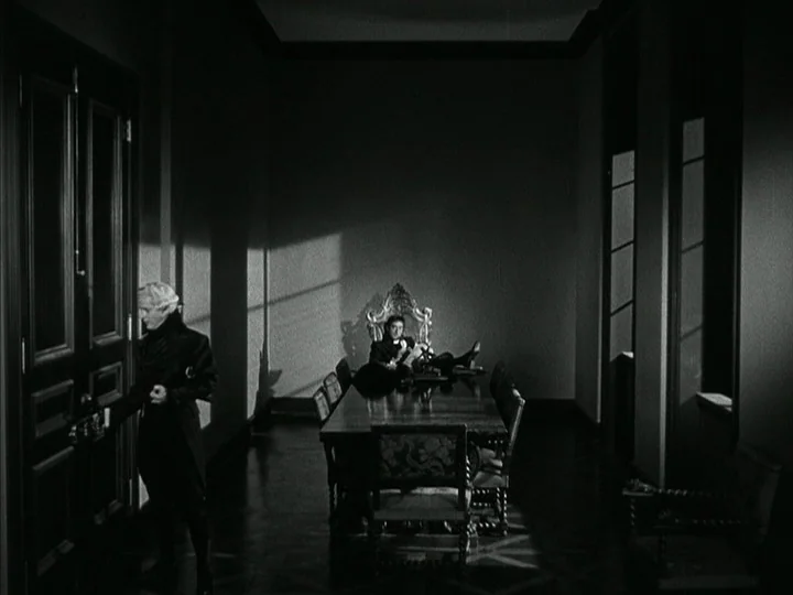 The Black Book (Reign of Terror) (1949) movie still: wide — A spacious room features a long wooden table and an ornate chair at the head. One man…
