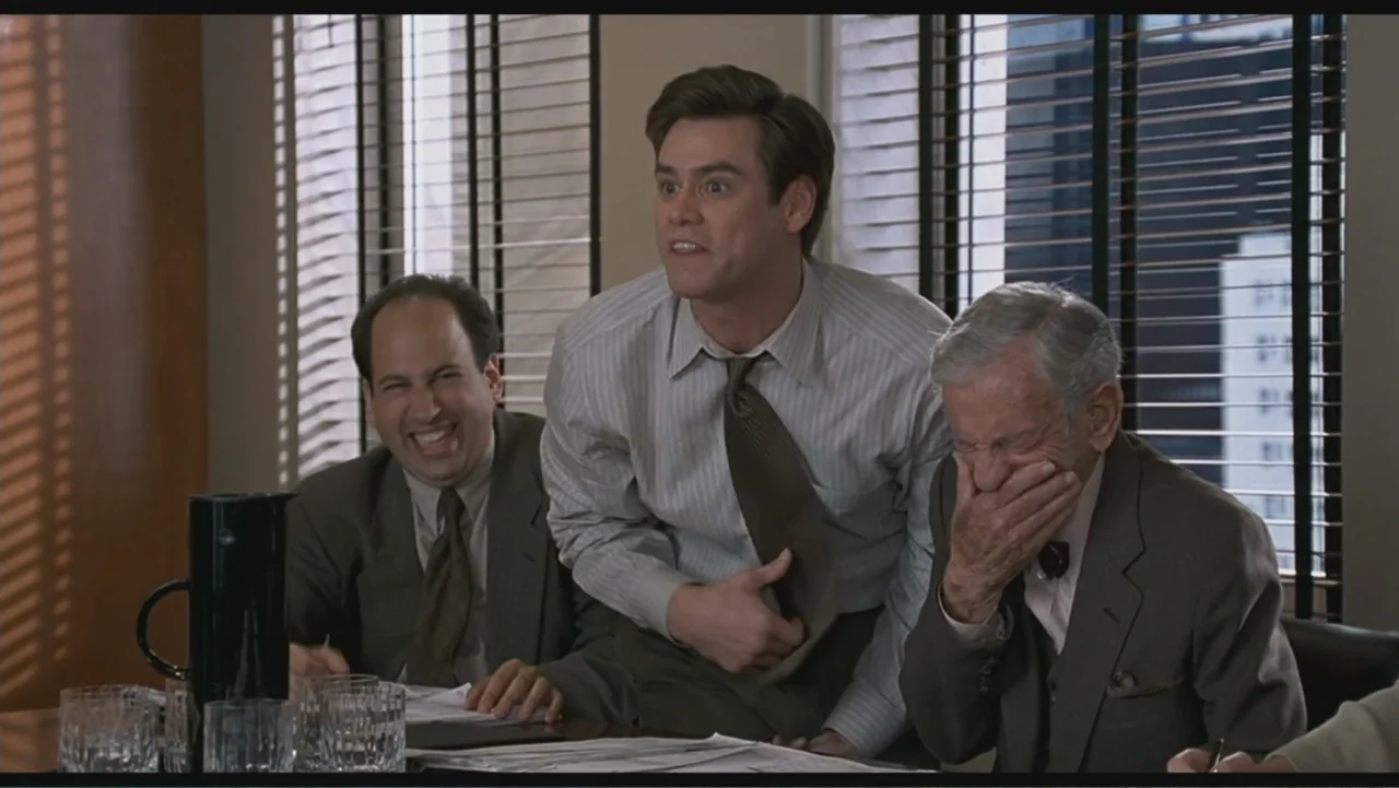 Liar Liar (1997) movie still: medium — A modern corporate board room with venetian blinds and stacks of paper on tables. Three men in professional…