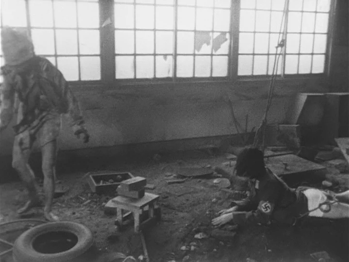 The War of Jan-Ken-Pon (1971) movie still: wide — A cluttered, debris-strewn industrial space features tall grid windows in the background. One…