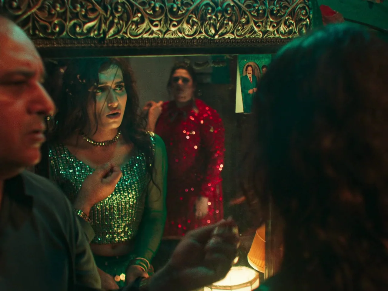 Joyland (2022) movie still: medium — A person examines their reflection in a large mirror with an ornate frame. Another individual in red attire…