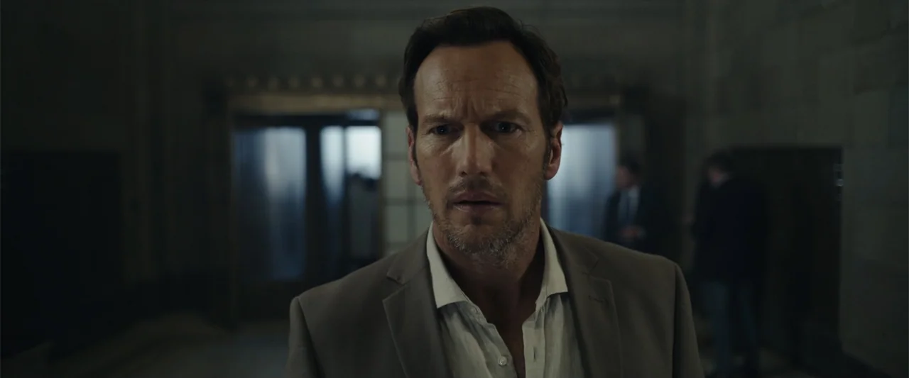 Moonfall (2022) movie still: medium — A dimly lit lobby features stone walls and blurred silhouettes of people in background. A middle-aged man in a…