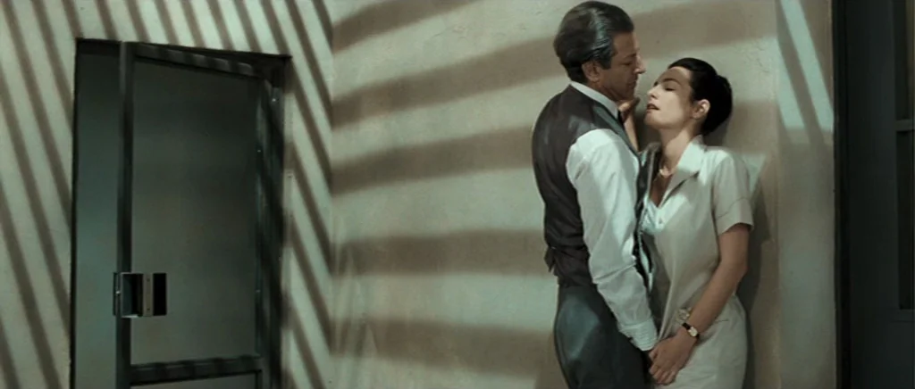 Adam Resurrected (2008) movie still: fullbody — A stark indoor space with a plain wall and a glass door. A man in a vest and a woman in a light…