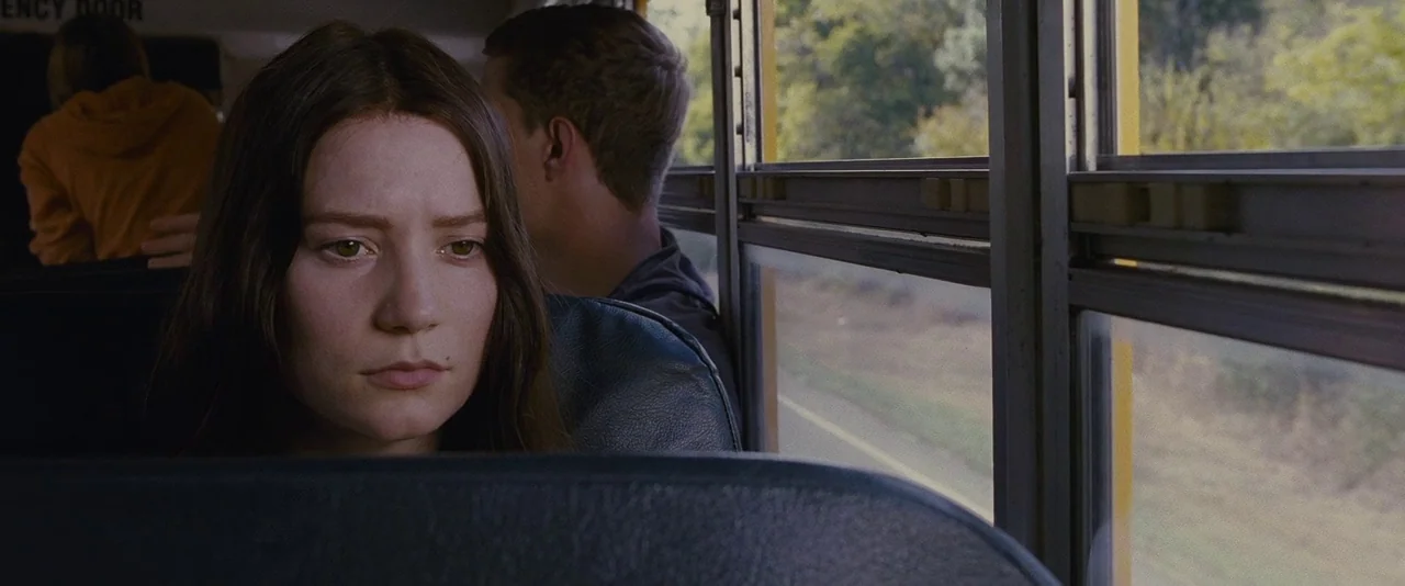 Stoker (2013) movie still: medium — Interior of a school bus with vinyl seats and large vertical window panes. A young woman sits in the foreground,…