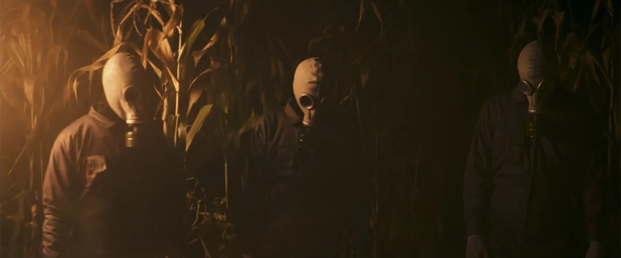 Treblinka's Last Witness (2012) movie still: medium — Three figures stand in a dense row of dark, nighttime corn plants. They wear gas masks and…