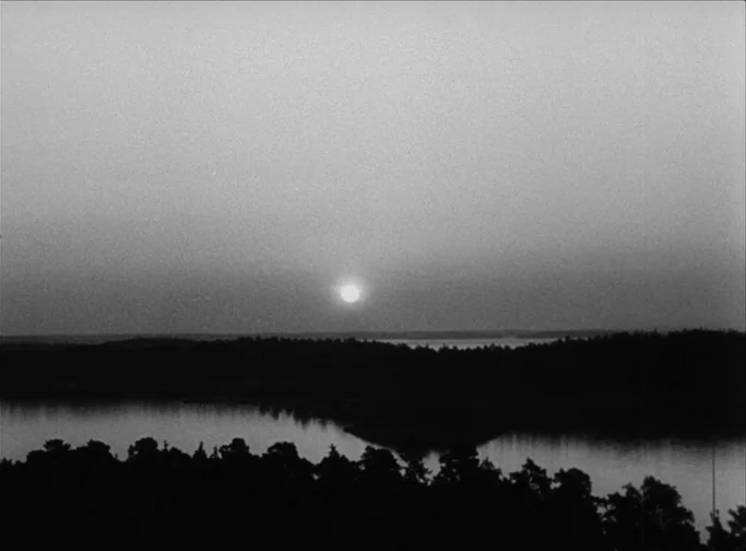 Summer Interlude (1951) movie still: establishing — A vast landscape shows a body of water bordered by dense silhouettes of trees. The sun sits low…