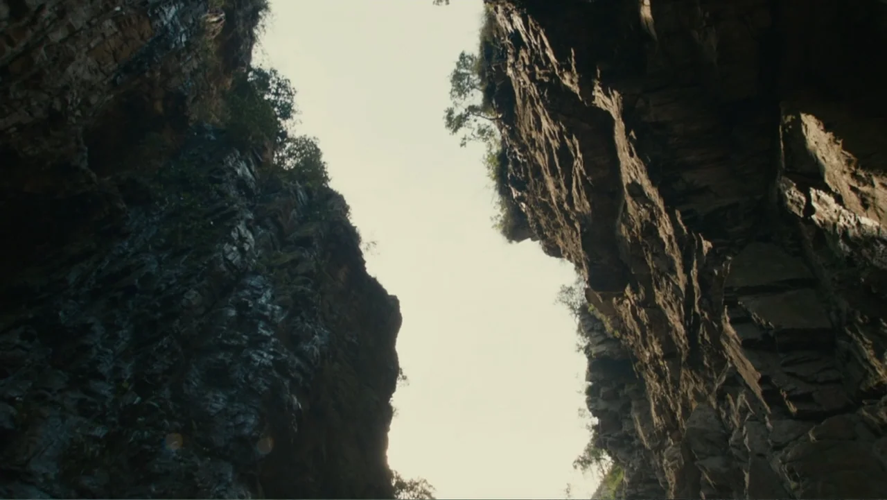 The Dinosaur Project (2012) movie still: establishing — A deep narrow canyon features vertical rock walls with minimal vegetation clinging to…