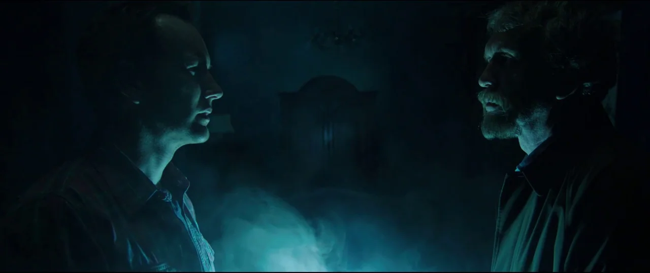 Insidious: Chapter 2 (2013) movie still: medium — Two men stand facing one another in a dimly lit, smoke-filled interior room. The space is heavily…